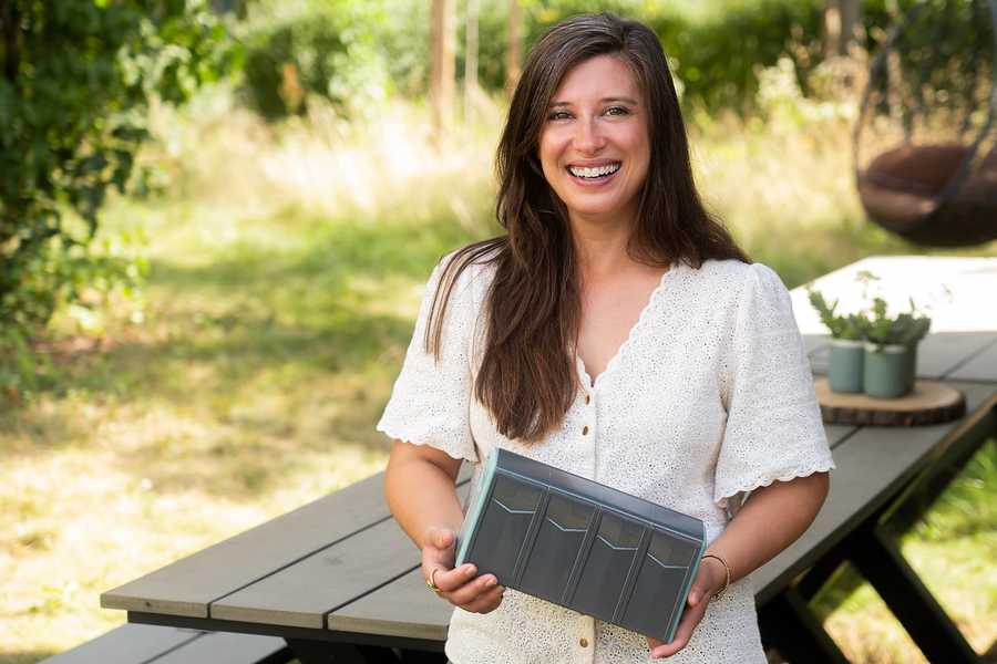 Eine junge Frau steht in einem Garten und lächelt in die Kamera. In der Hand hält sie die Miniatur einer Fahrradbox.